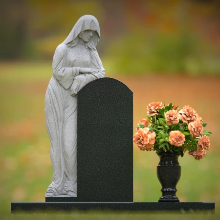 Praying angel sculpture resting beside floral tribute on classic headstones.