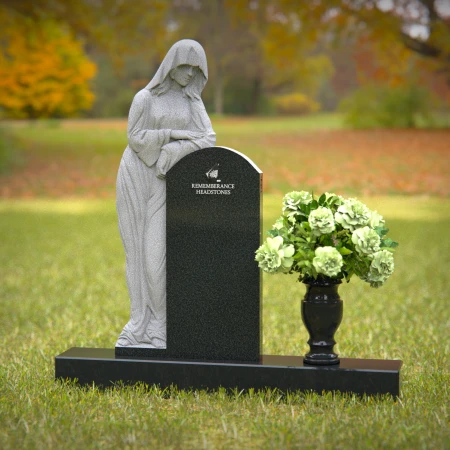 Praying angel sculpture resting beside floral tribute on classic headstones.